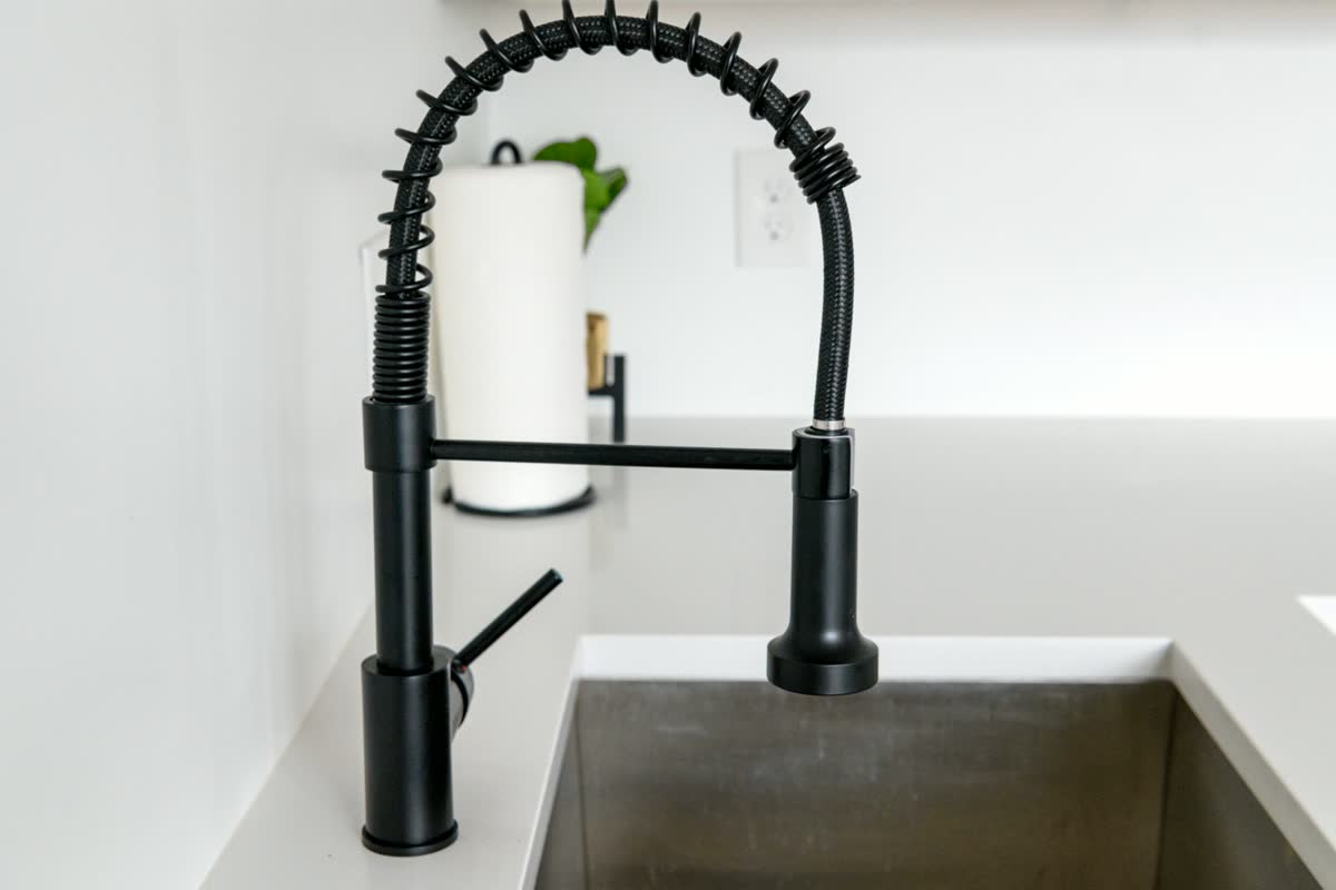 A matte black kitchen mixer tap over a steel sink